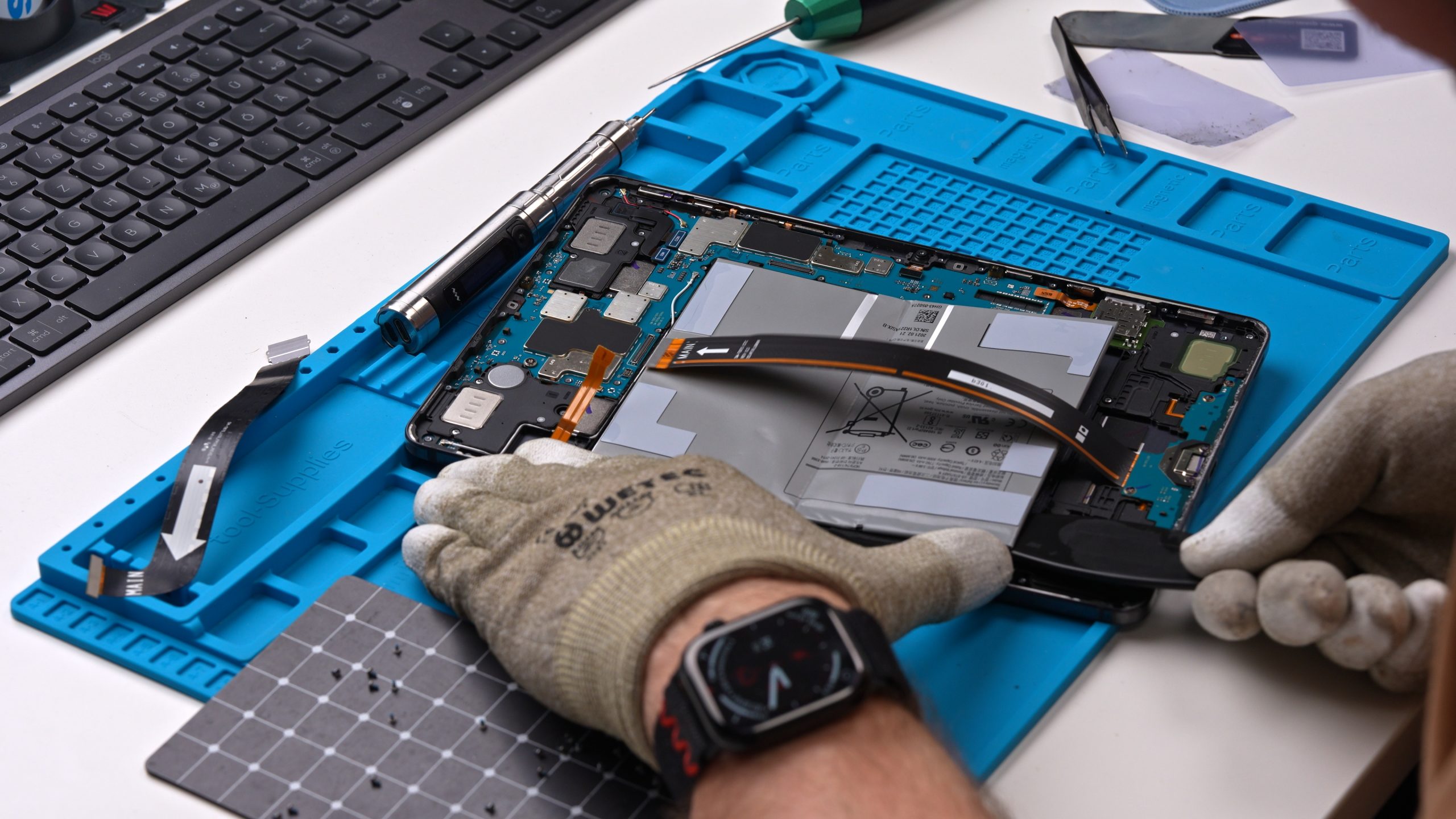 Tablet-Ipad-Reparatur Ein geöffnetes Samsung Tablet liegt auf einer blauen Werkstattmatte; der Akku ist sichtlich aufgebläht und wird von einem Techniker fachgerecht für den Austausch vorbereitet.